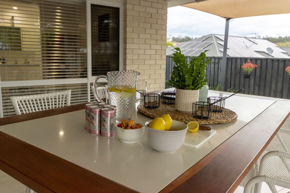 Outdoor dining table set with drinks and snacks on covered patio.