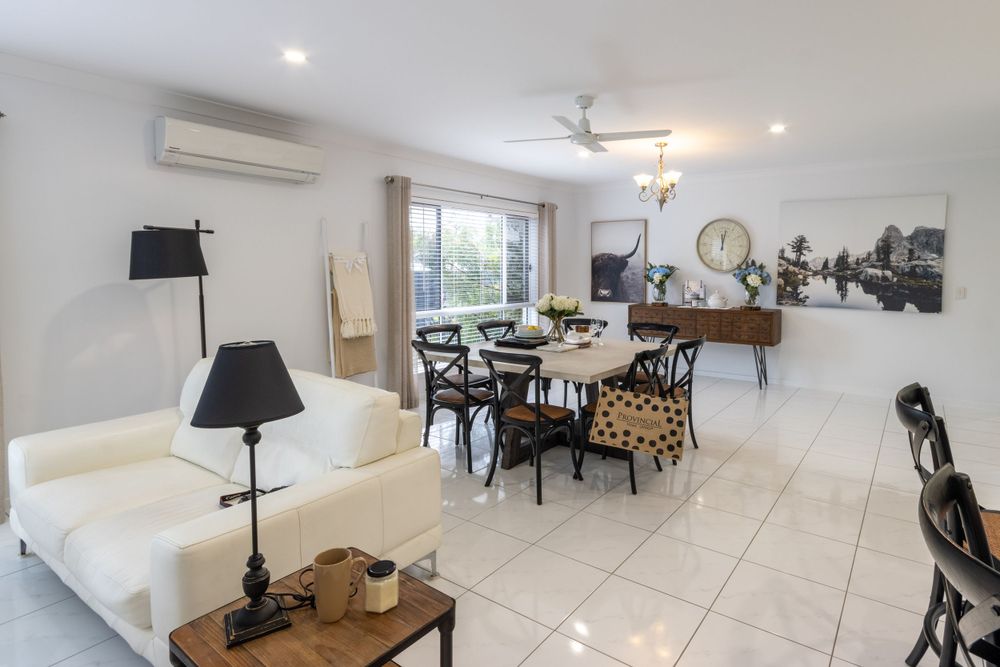 Open plan living room with white sofa, dining set and modern decor in bright interior space.