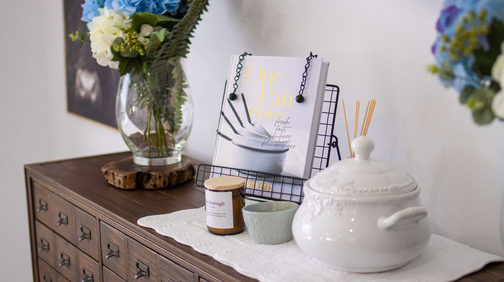White ceramic tureen and vase with blue hydrangeas on a dresser with organizational items.