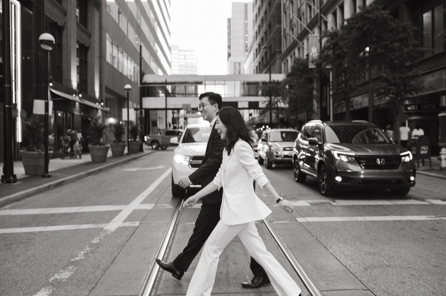 Black and white photo of couple dancing in city street with urban buildings in background.