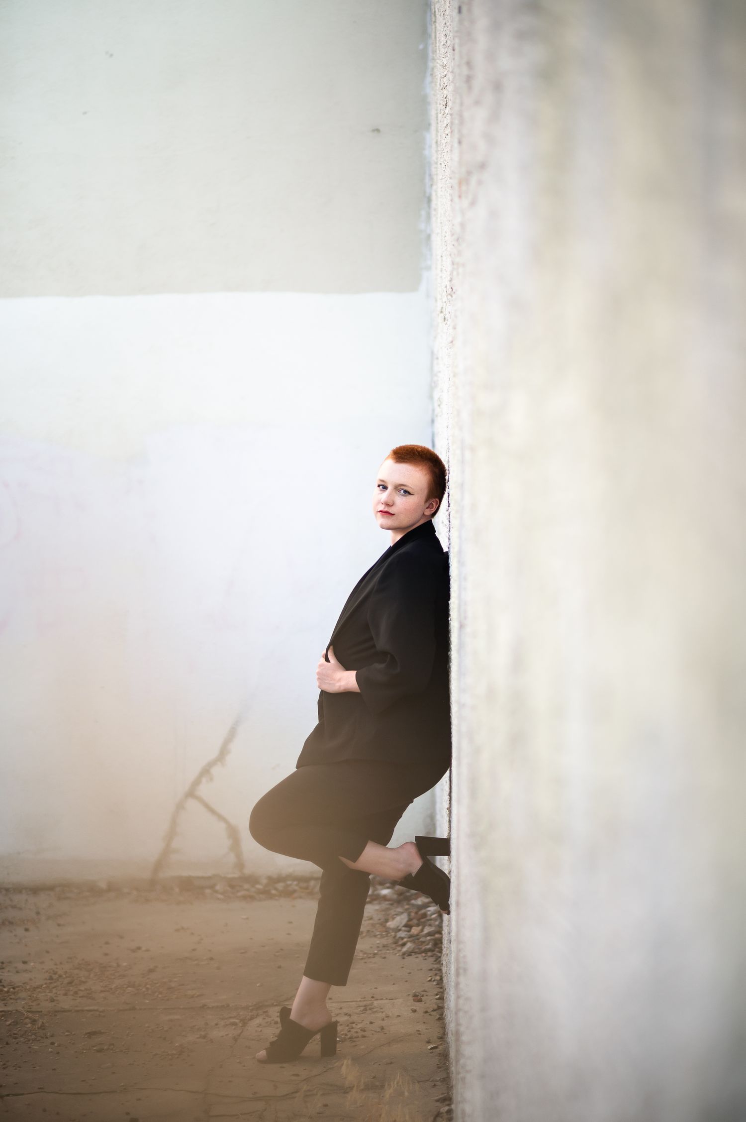 Artistic portrait of person in black outfit leaning against white wall.