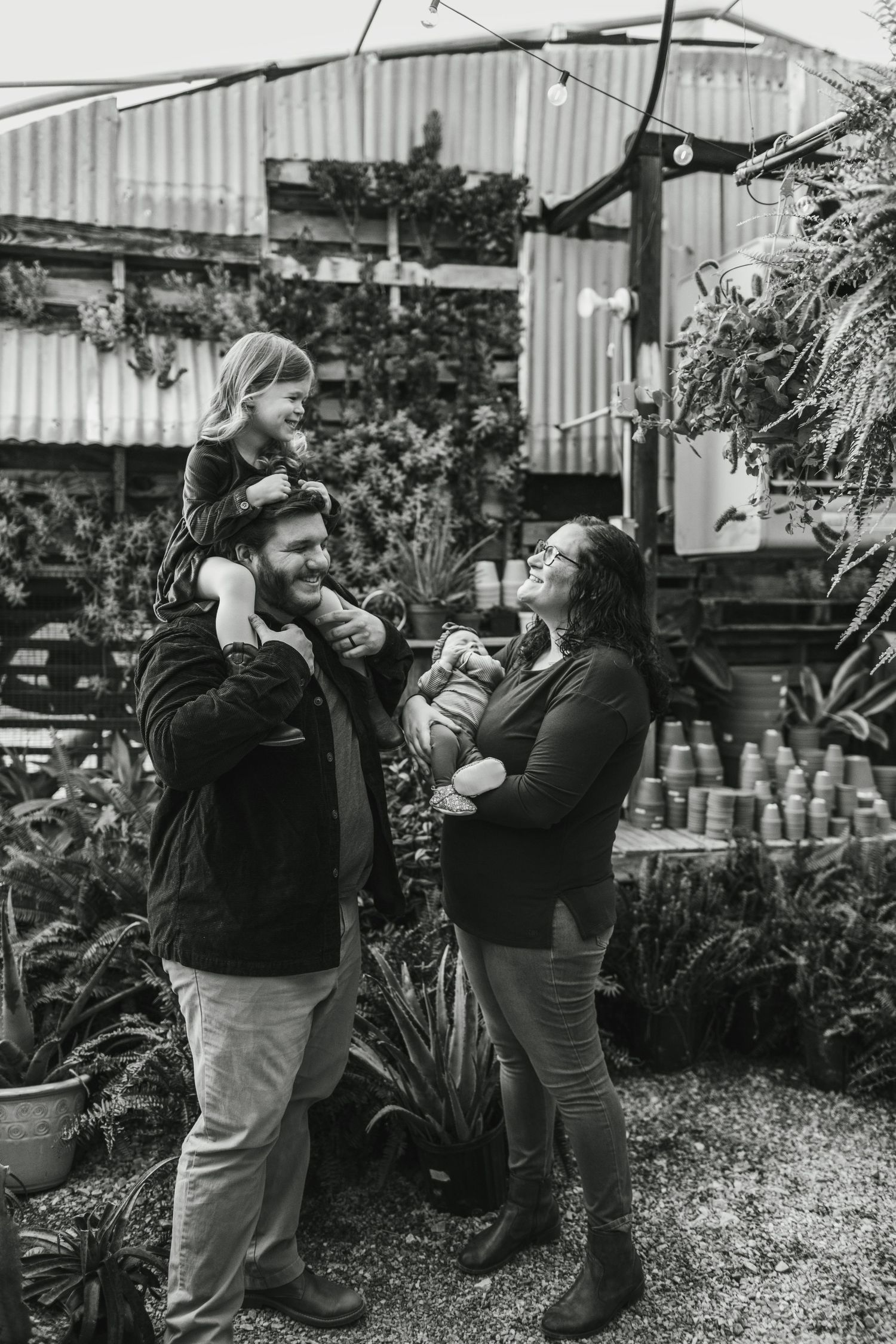 Family enjoying time together in a garden setting with plants and corrugated metal walls in the background.