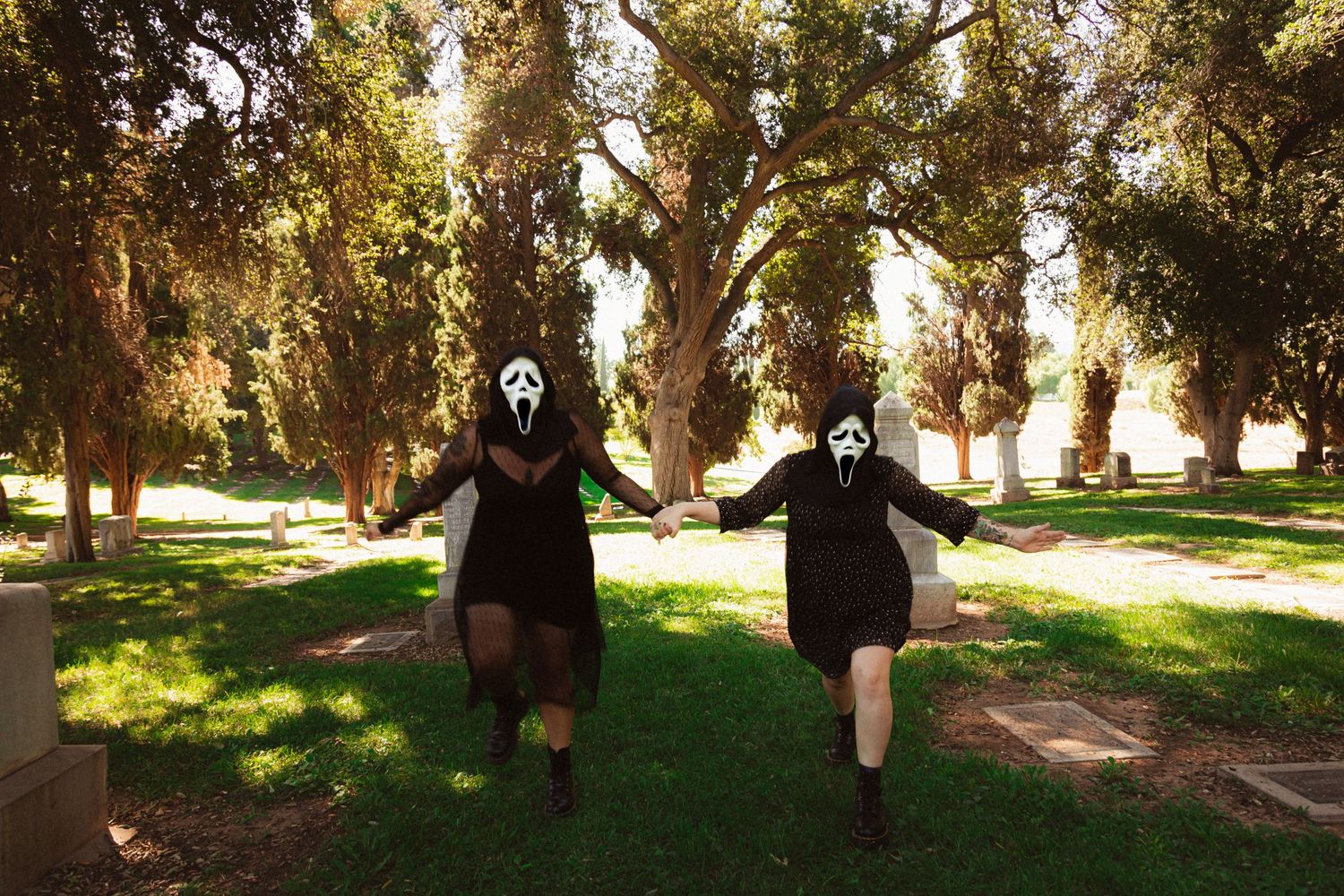 Two people in ghost masks running through a park with trees in the background.