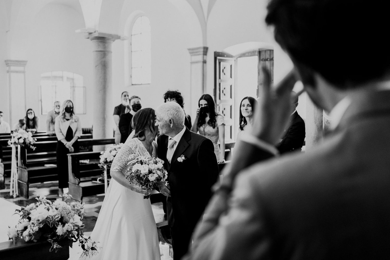 Black and white photo of a bride walking down the church aisle with her father during a wedding ceremony.