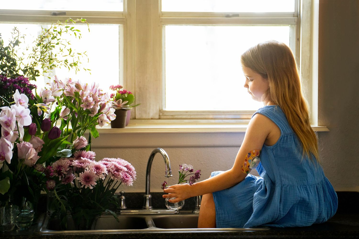 Young girl in blue dress sitting on counter watering flowers in home photography Ft Sam Houston in San Antonio Texas