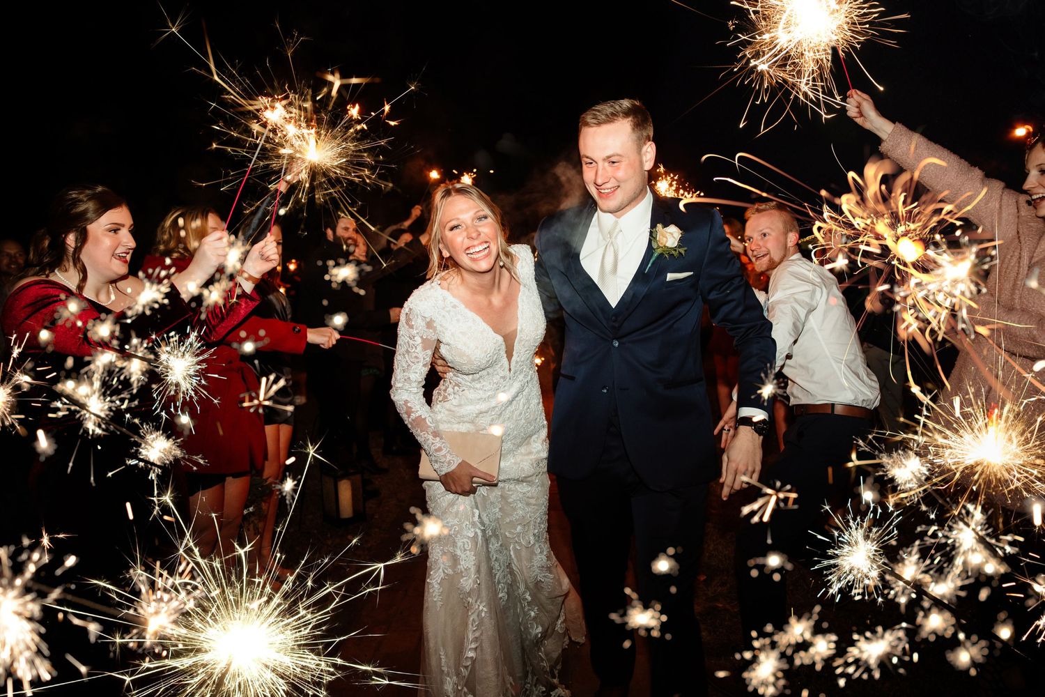 Newlyweds exit their wedding celebration through a tunnel of sparklers at night.