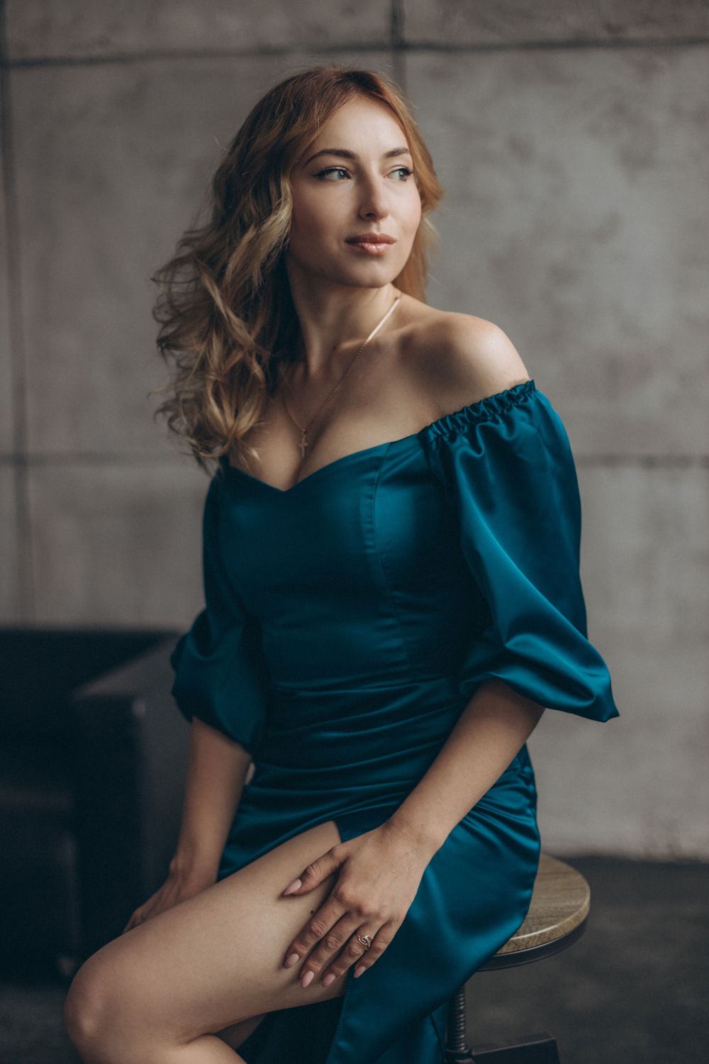 Glamour portrait in deep teal off-shoulder dress with soft styling against concrete backdrop.