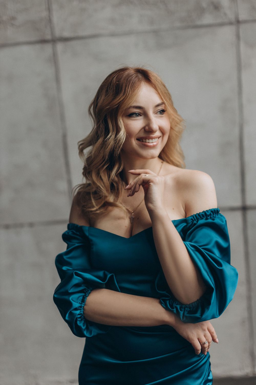 Elegant portrait in teal off-shoulder dress against industrial concrete background.