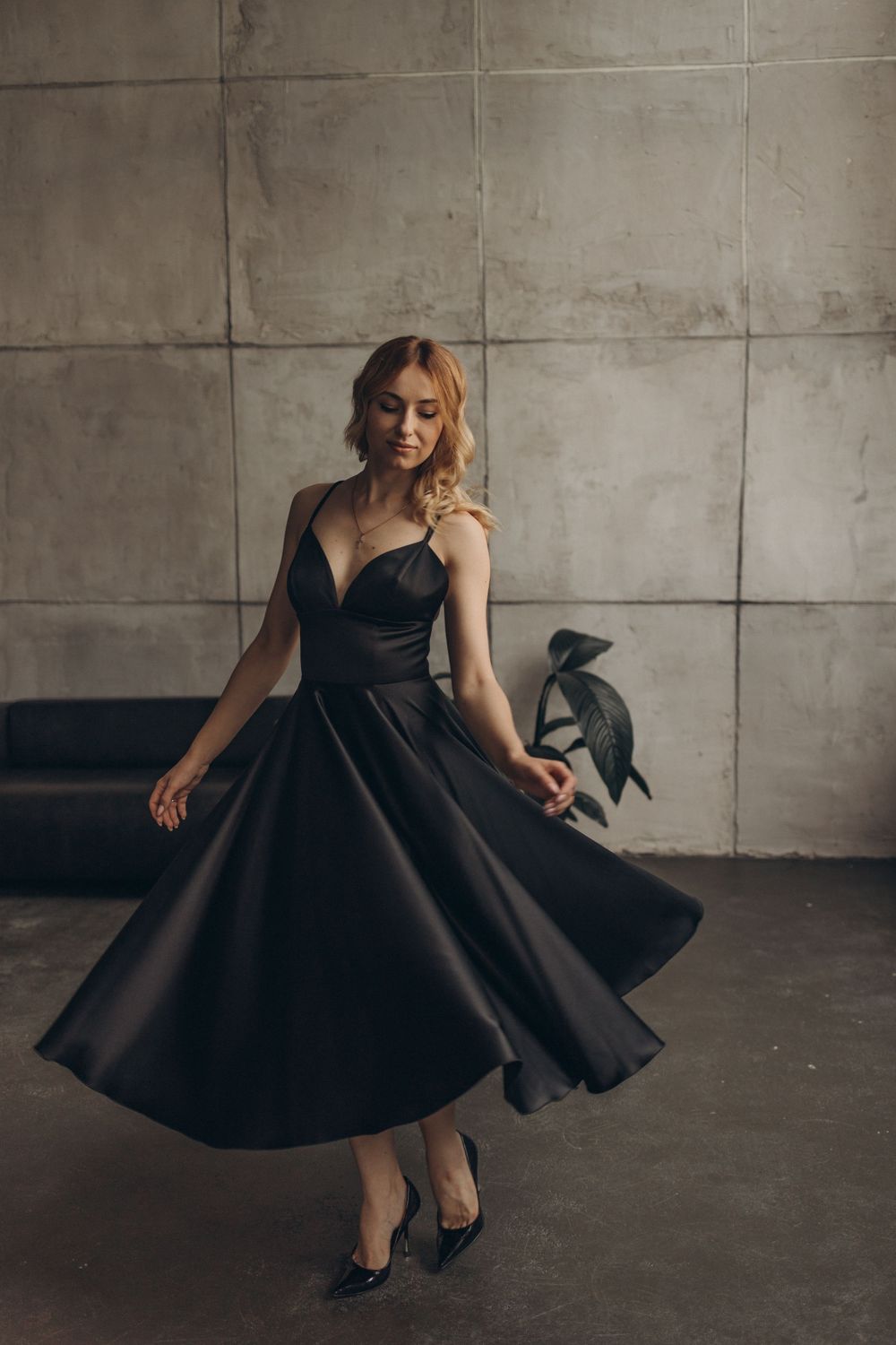 Elegant twirling motion in black formal dress against industrial concrete wall background.