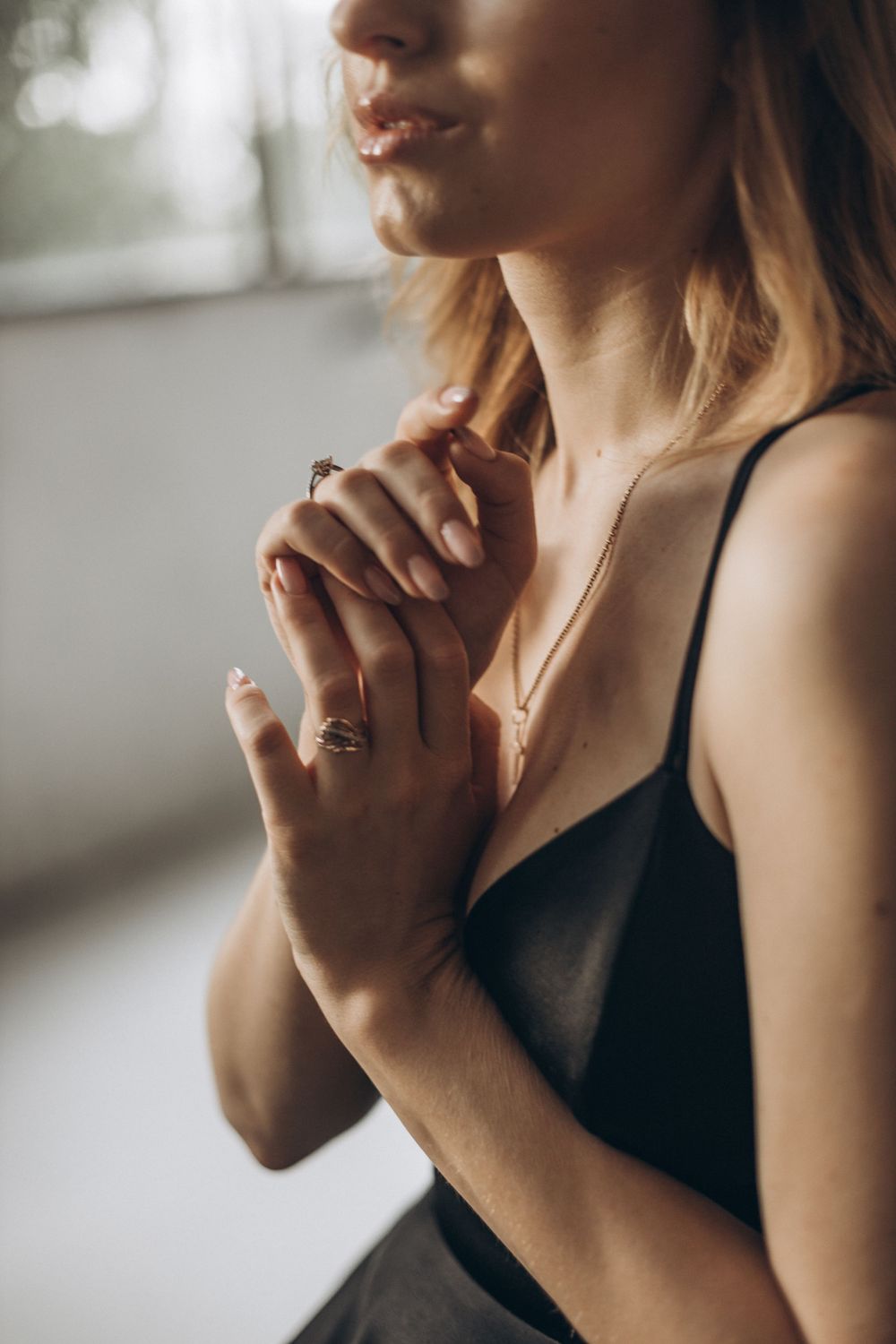 Close up profile view showing clasped hands and delicate jewelry in natural window light.