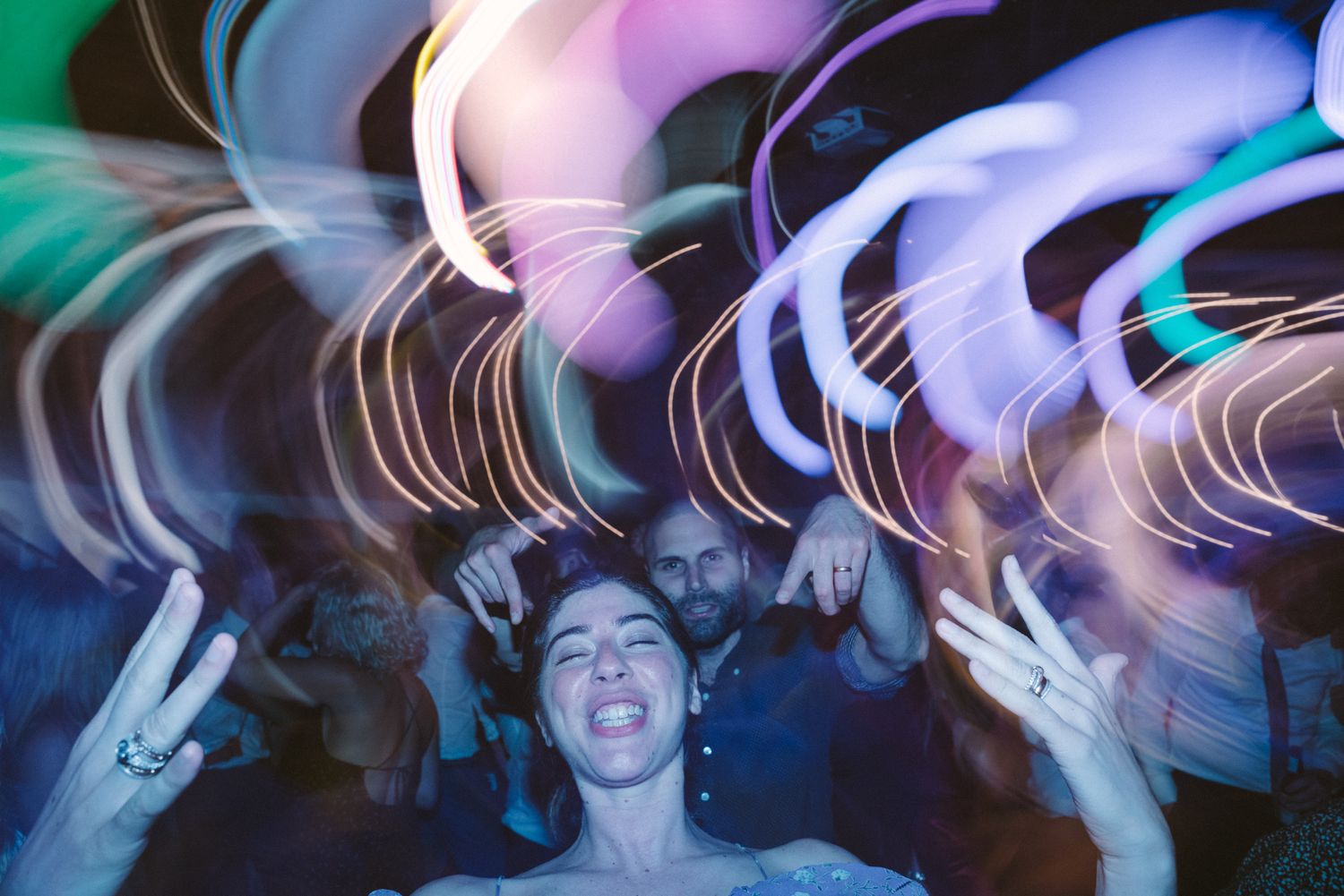 Colorful light trails and motion blur create an abstract pattern at a nighttime dance party.