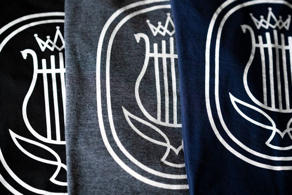 Repeating lyre logo design printed in white on dark fabric.