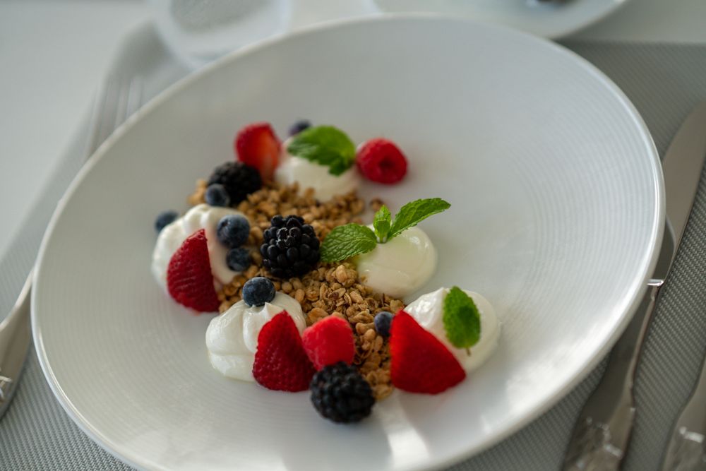 Elegant dessert plate with fresh berries, cream and granola on white dish.