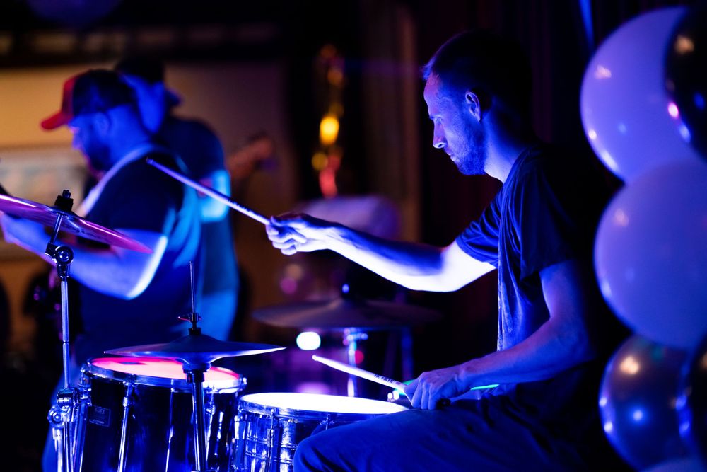 Drummer playing lit by blue stage lights with balloons visible in background.