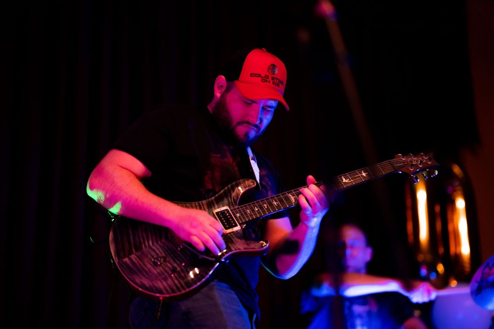 Guitarist performing on stage bathed in dramatic red lighting during a live music performance.