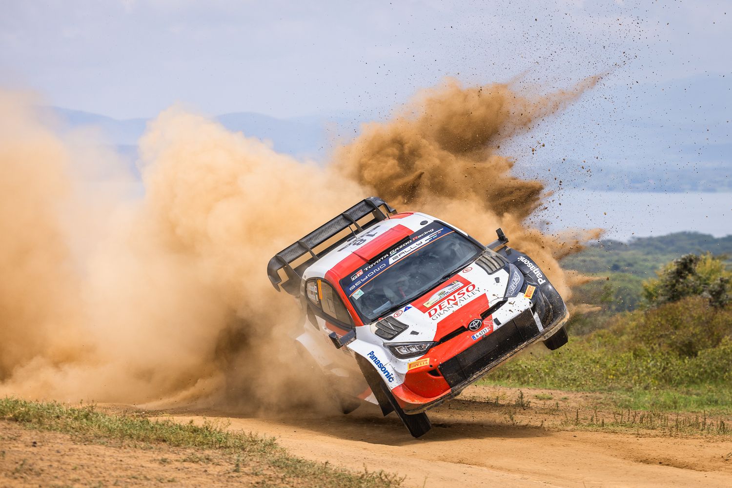 Rally car jumps through the air creating a massive dust cloud on dirt track.