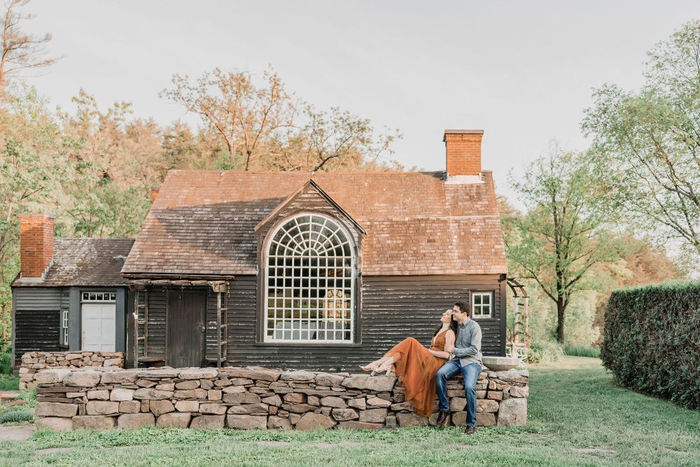 couple sitting on old stone wall in front of rustic wedding venue in Maine