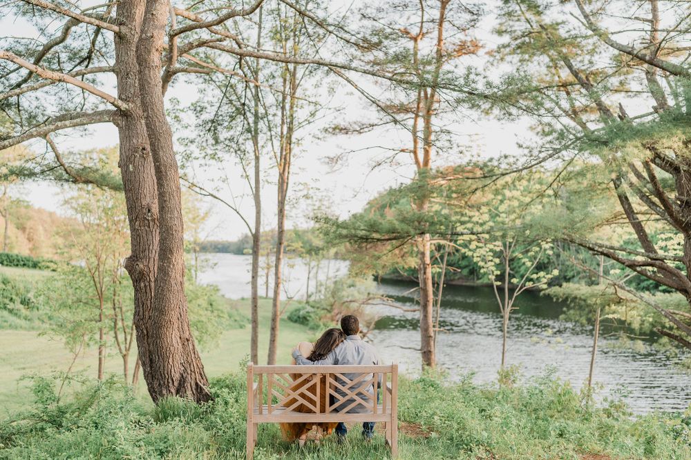 woman leaning on shoulder of man while sitting on bench facing waterfront at Maine wedding venue
