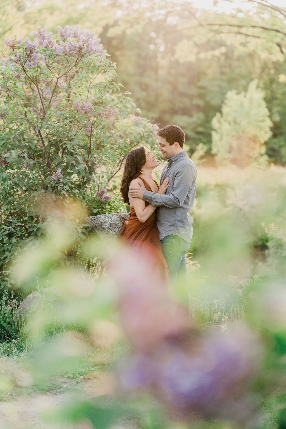 man and woman looking at each other with lilac flowers around them at Maine engagement session