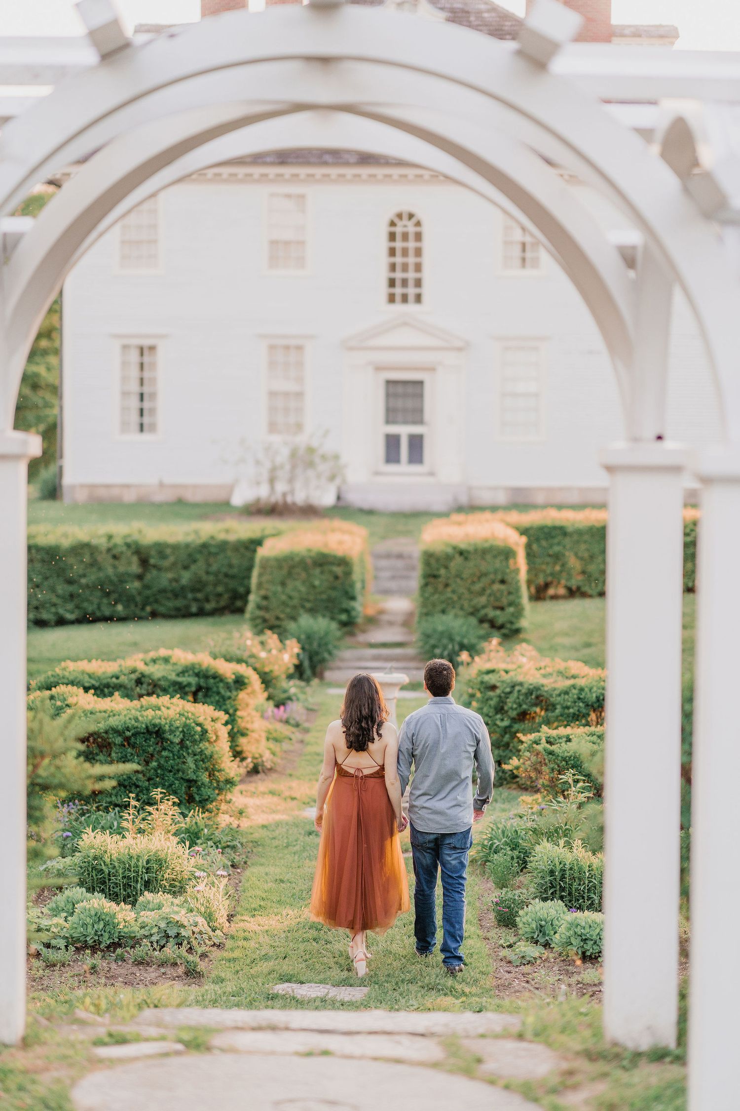back of couple walking through garden at Hamilton House in Maine during summer engagement session