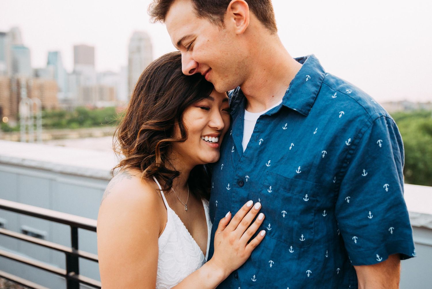 Bi-racial couple poses for engagement portraits with Minneapolis skyline behind them.