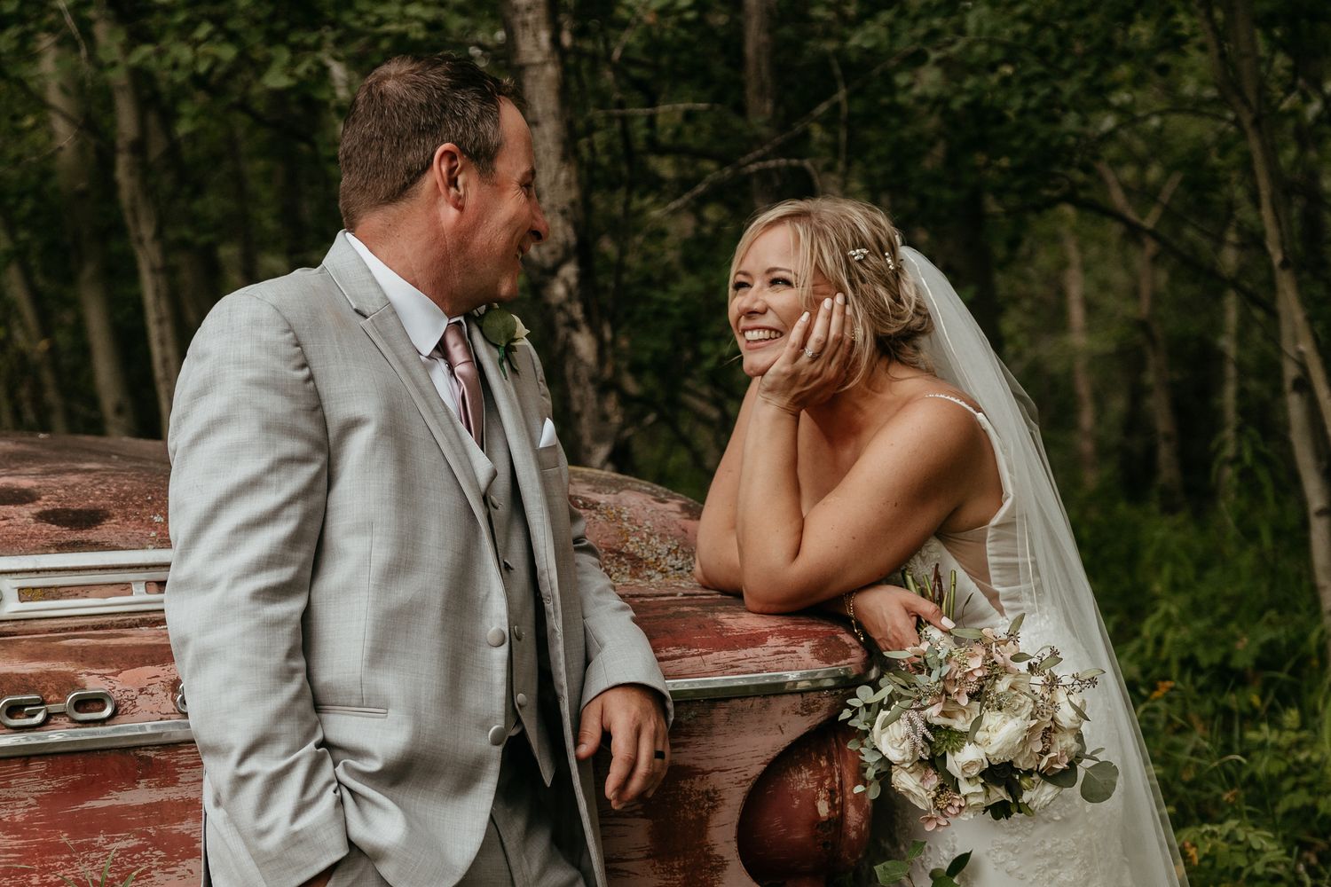 Bride and groom sharing a candid moment by vintage red truck in forest setting.