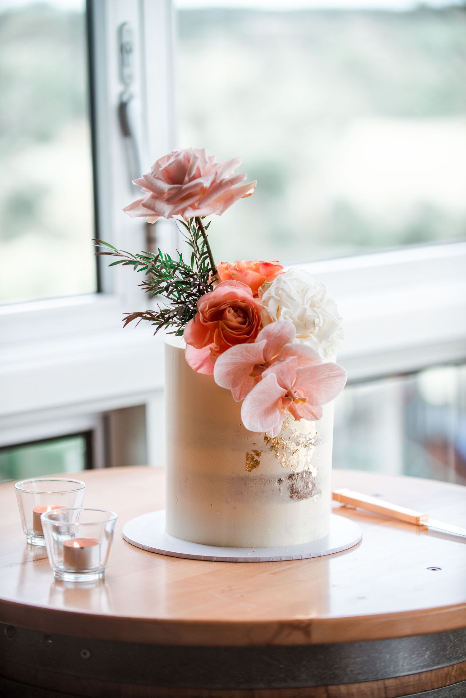 Simple white wedding cake decorated with coral and pink flowers on a wooden table.