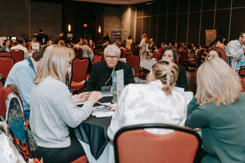 Corporate event attendees participating in a discussion session at tables in a dimly lit conference room.