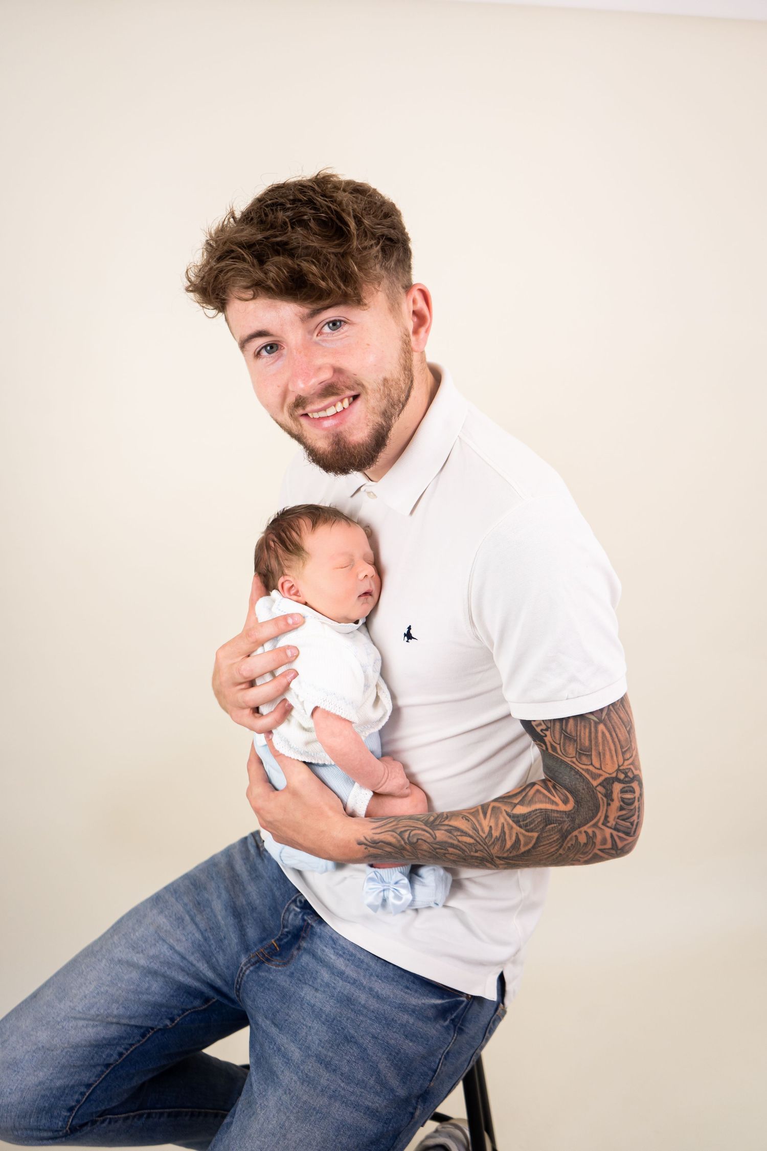 Father wearing white polo, holding sleeping baby for parent photos at newborn photoshoot in Doncaster.