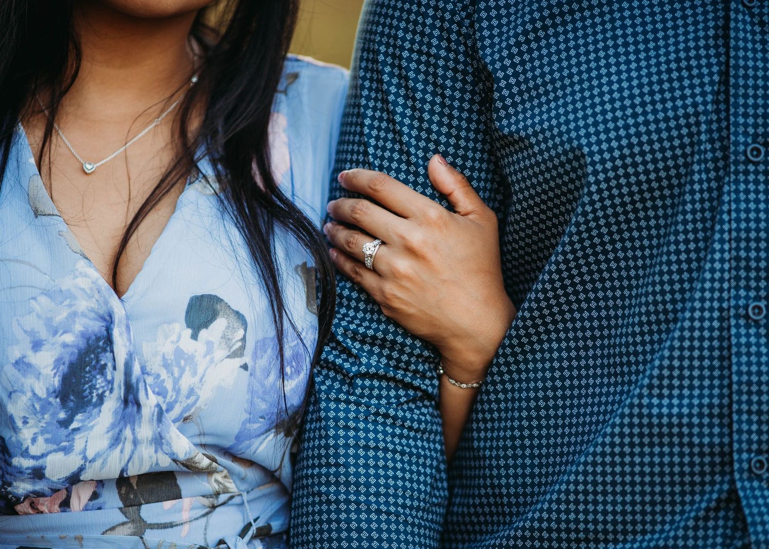 Close-up of couple embracing showing engagement ring on woman's hand wearing a floral blue dress.