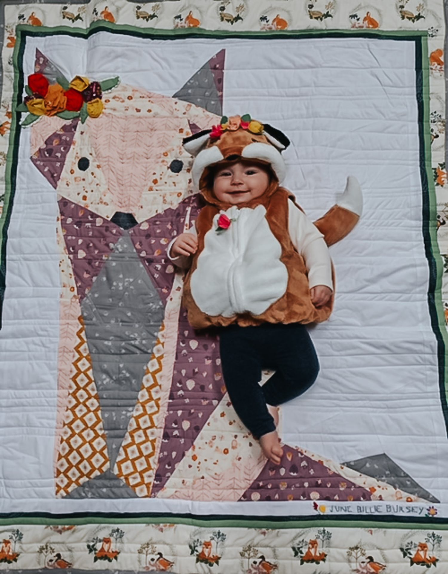 Love quilt with a fox on the face and a baby dressed as a fox laying on it.