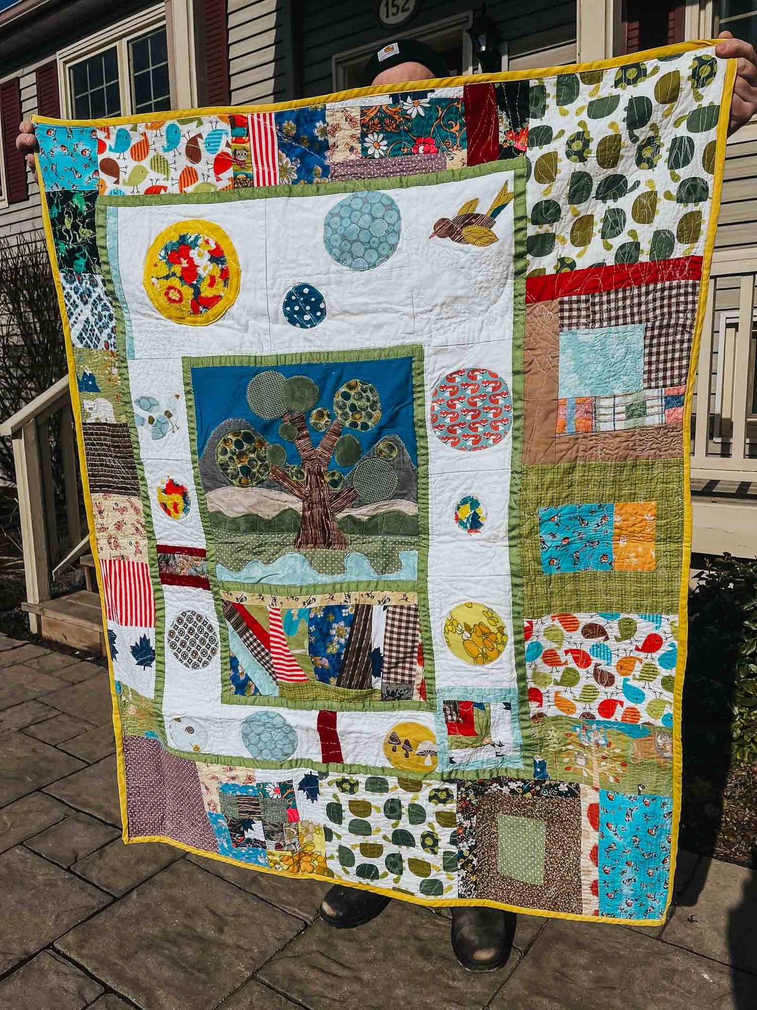Love quilt made with fabric from a number of different people, there's a tree in the middle.