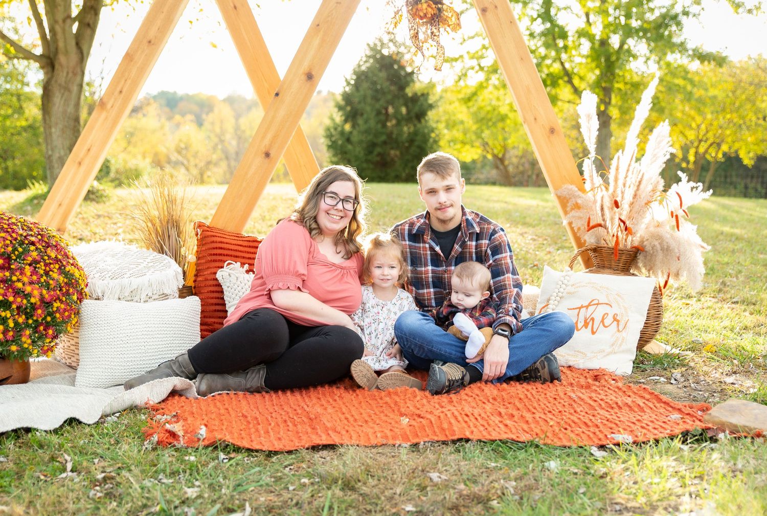 Couple sits on orange blanket with fall decor during outdoor photo session.