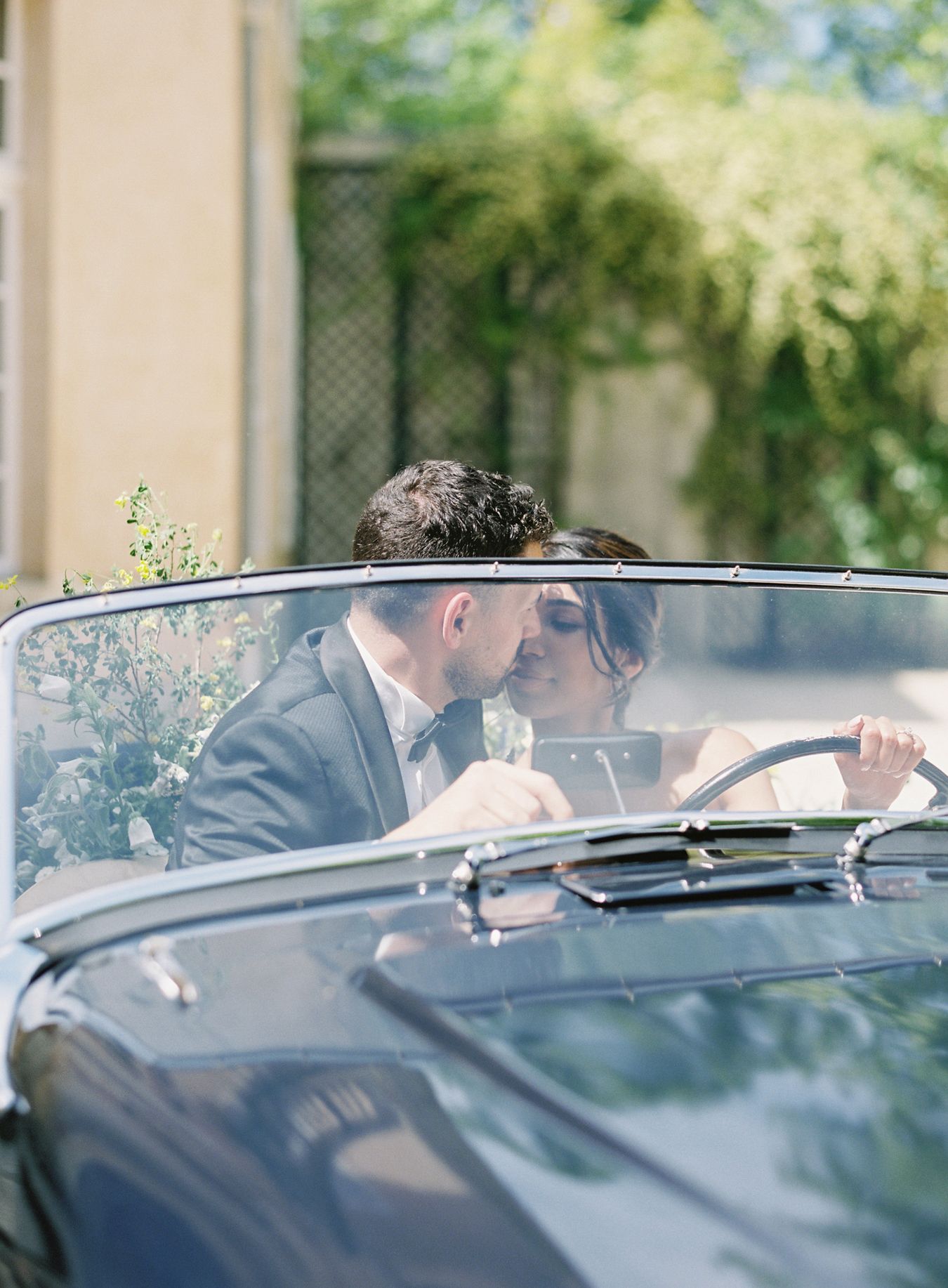 Vintage convertible car with wedding decorations in front of elegant mansion.