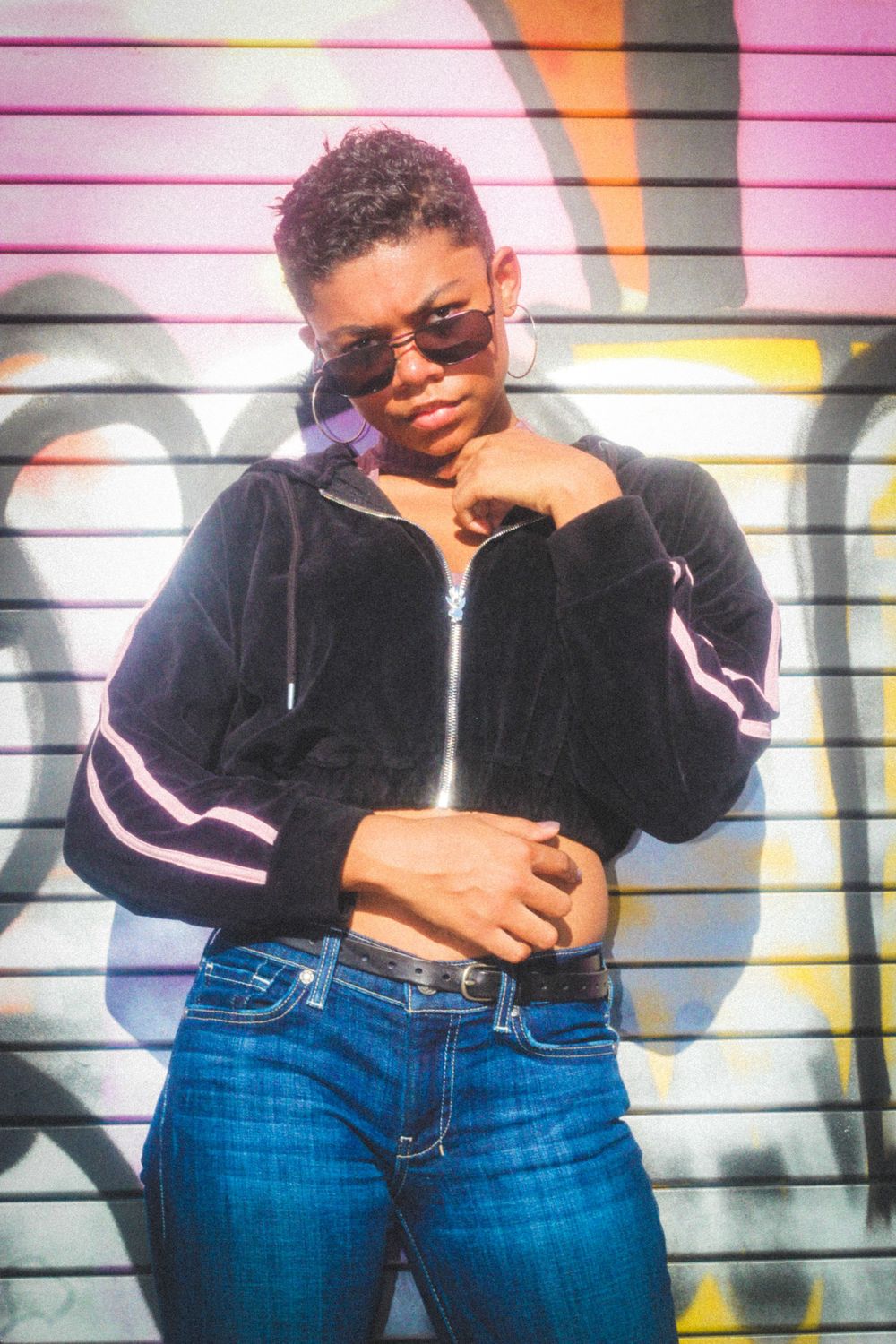 Fashion portrait against graffiti wall wearing black jacket and sunglasses.