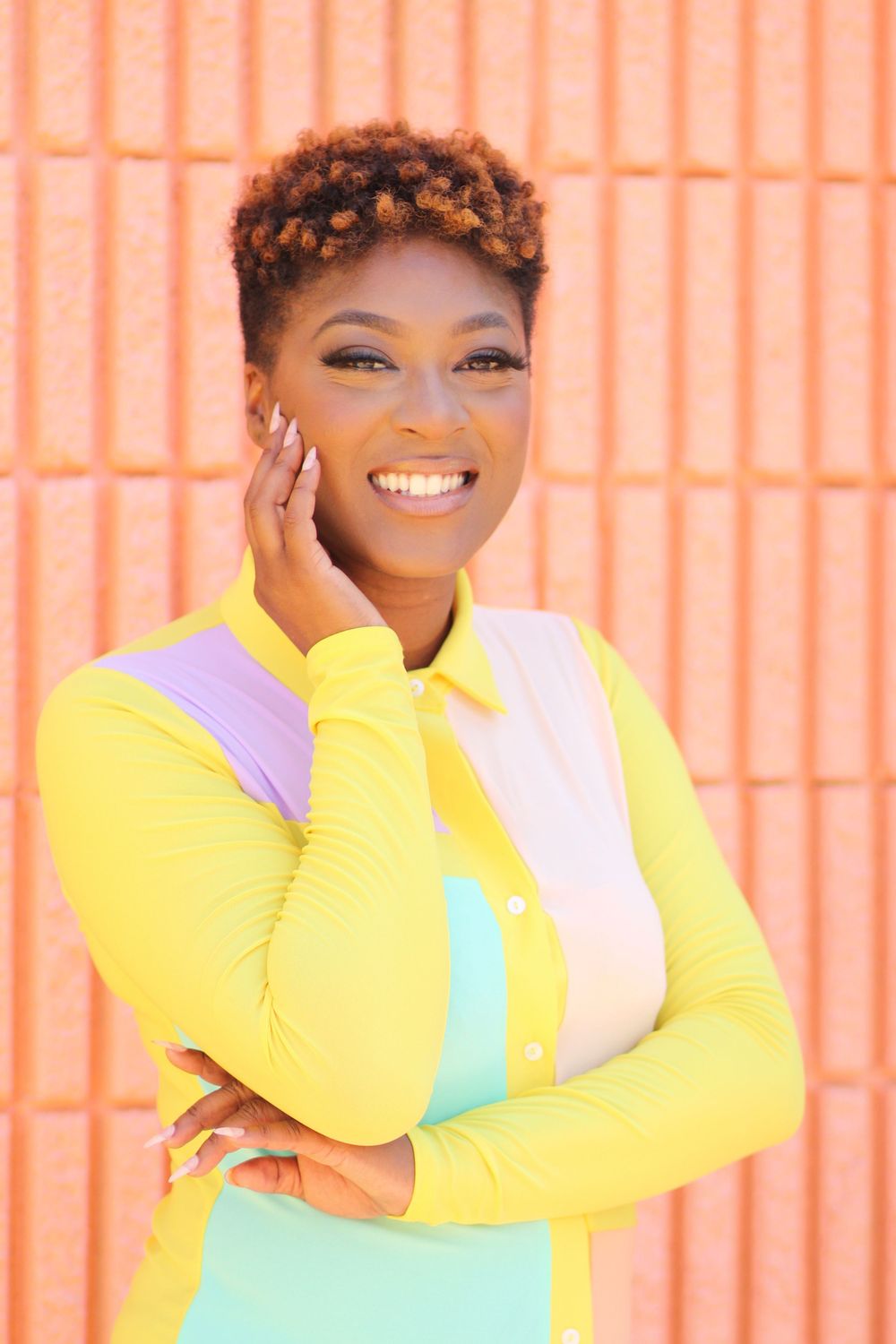 Person in colorful yellow and pastel outfit posing against orange wall.