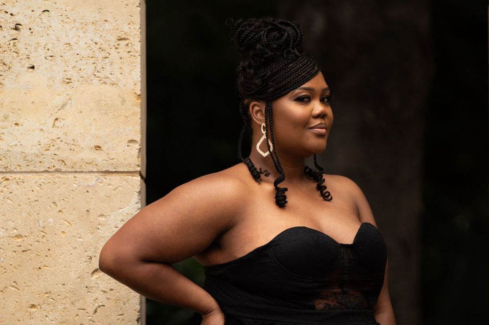 Glamorous portrait of woman in black formal dress against light stone background.