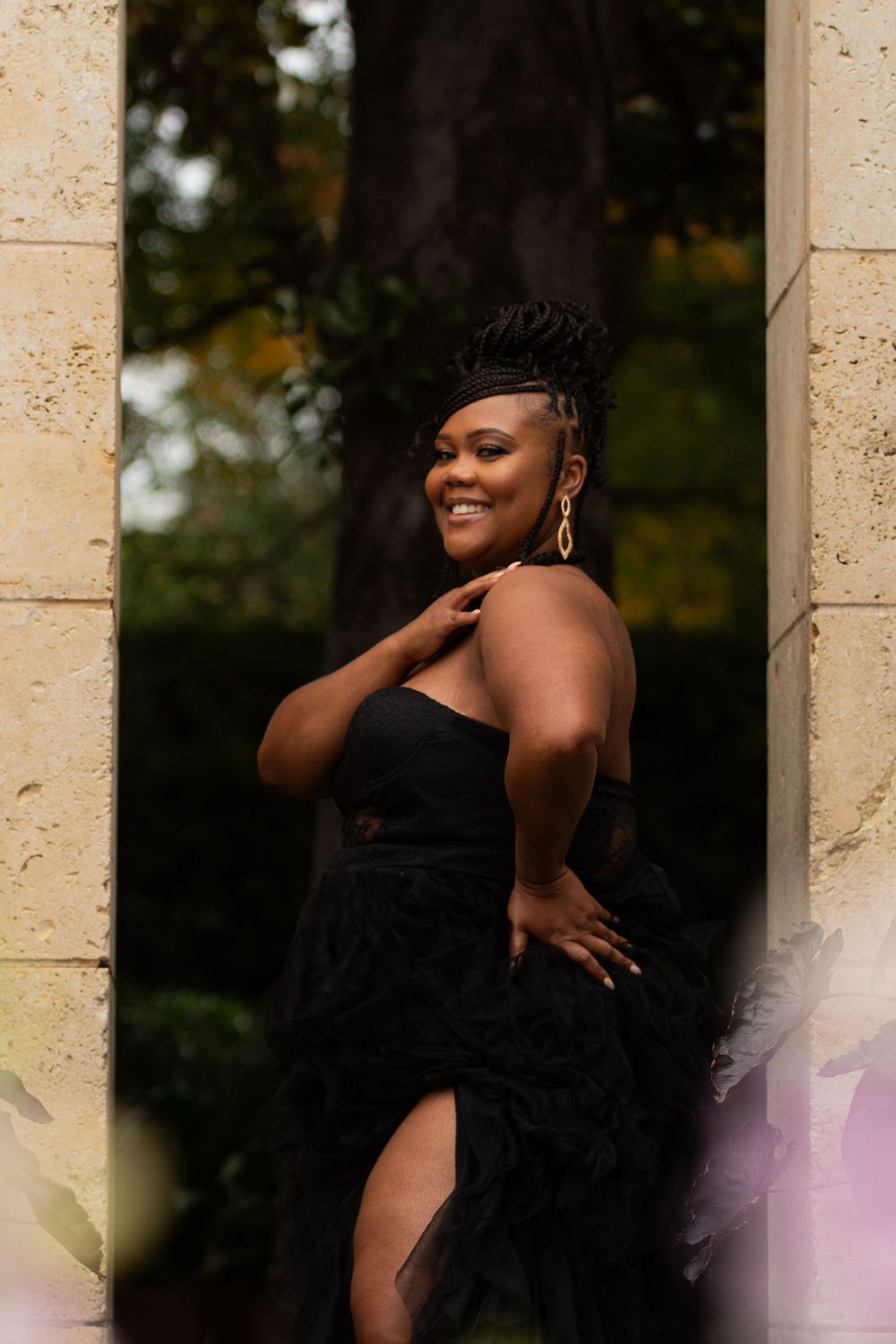 Elegant portrait of woman in black dress posing against stone pillars outdoors.