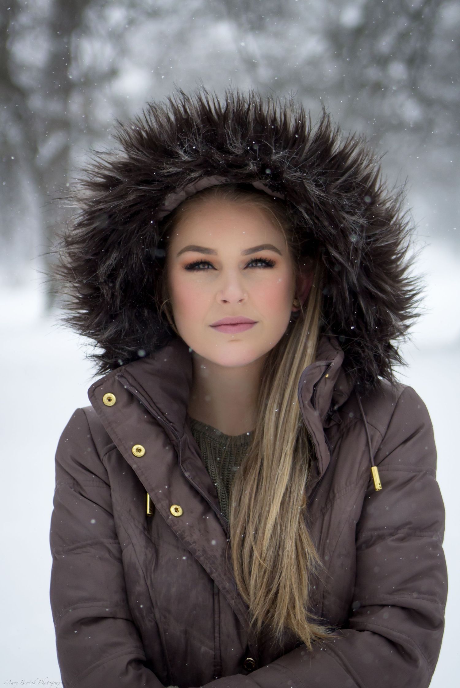 Young woman in fur-trimmed winter coat standing in snowy outdoor setting.