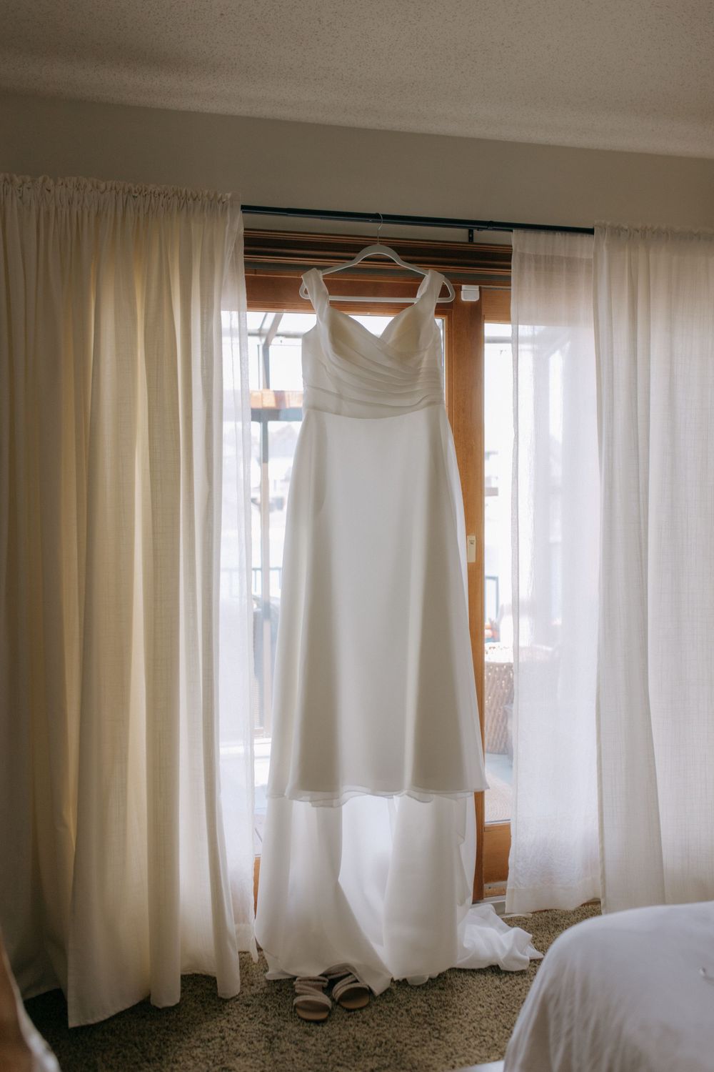 White wedding dresses and formal attire hanging from a curtain rod in natural light.