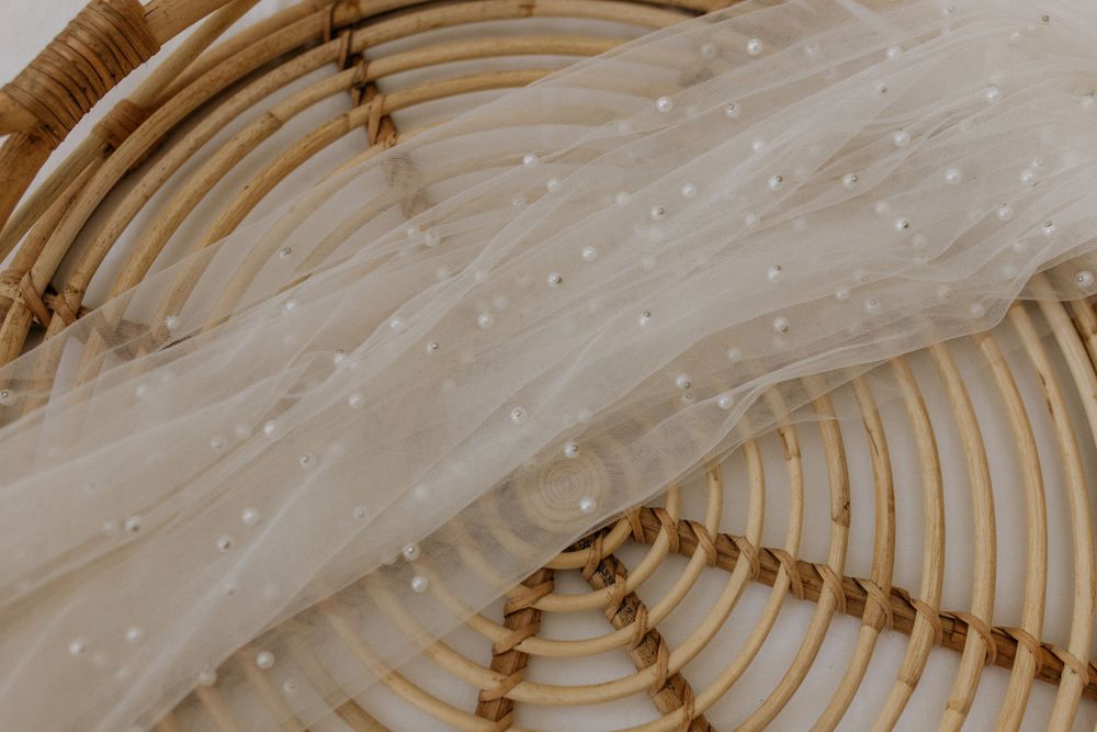 Close-up of wedding veil with scattered pearl embellishments on bamboo surface.