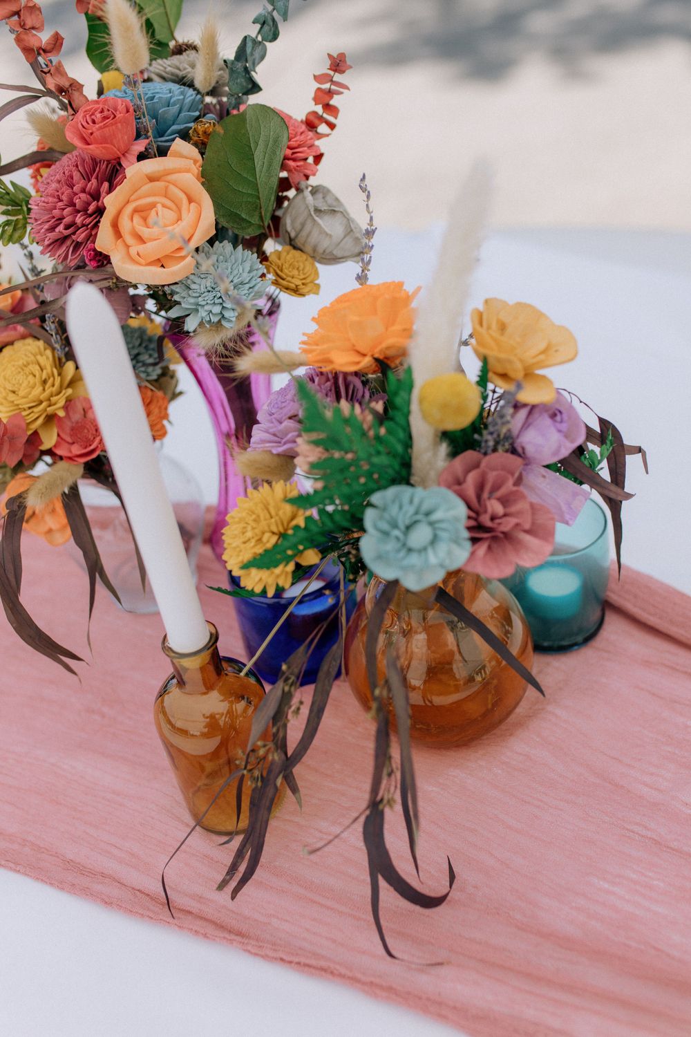 Vibrant floral centerpieces with pink, orange, and blue blooms displayed in amber and blue glass vases.