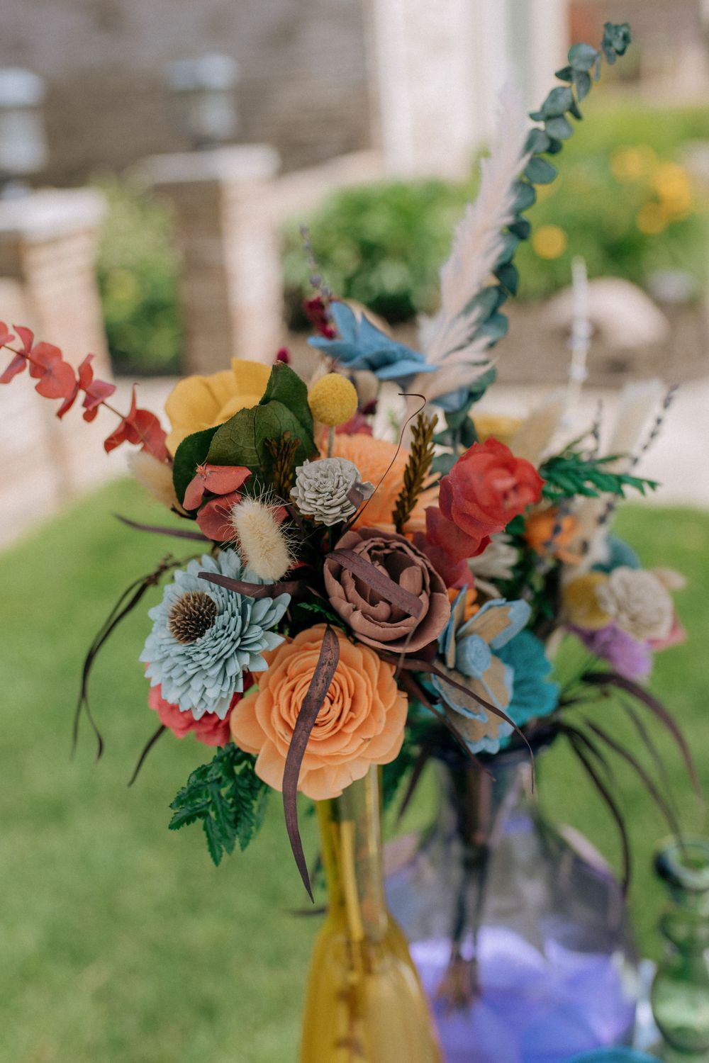 Artistic floral arrangements with colorful blooms displayed in glass bottles against a natural outdoor backdrop.