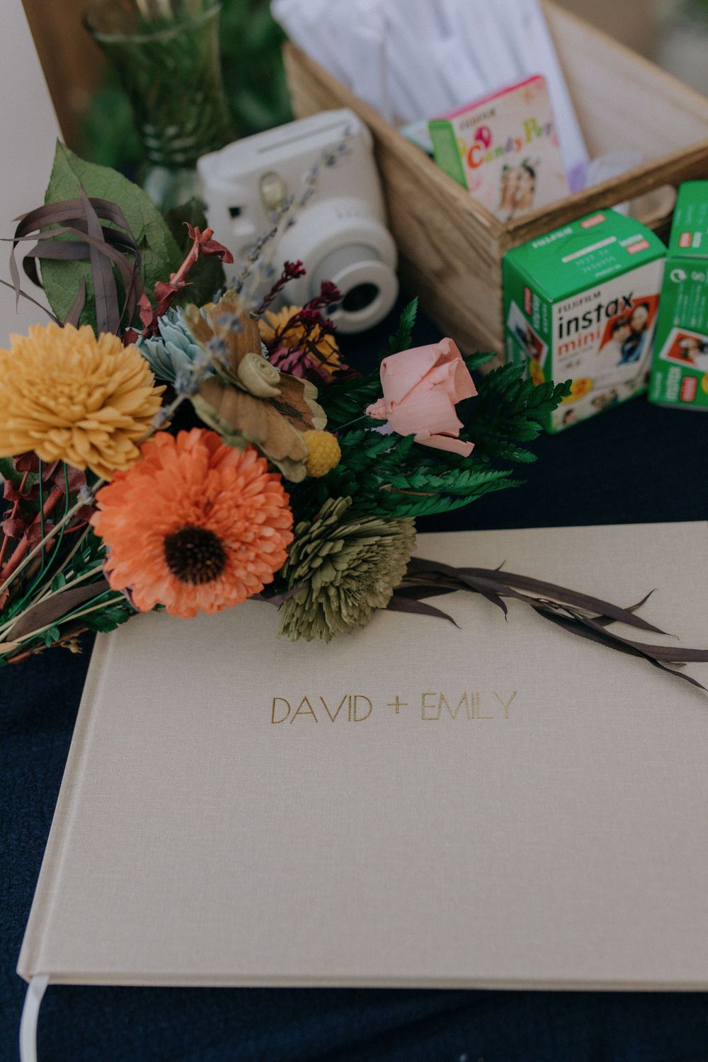 Wedding album with florals and Instax camera setup on dark blue surface.