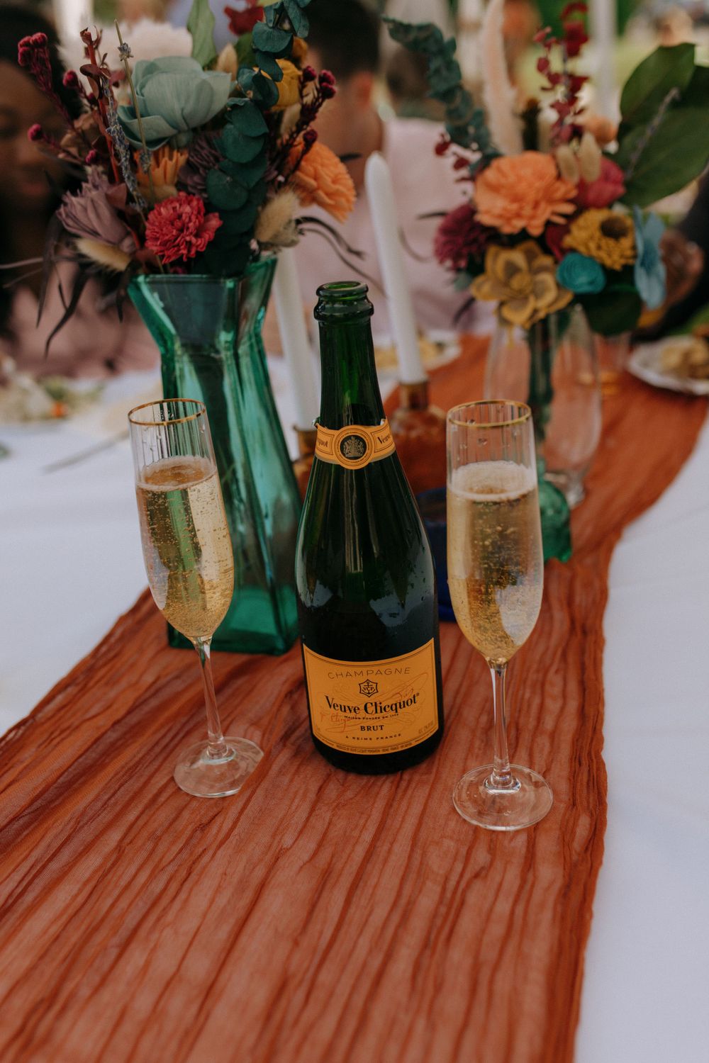 Champagne setup with Veuve Clicquot bottle and flutes next to colorful floral arrangements.