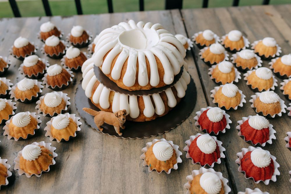 White bundt cake and mini desserts arranged on wooden surface at wedding reception.