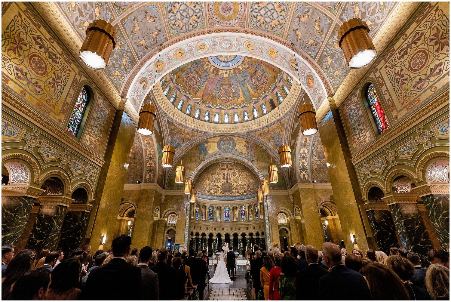Grand church ceremony with ornate domed ceiling and gathered guests in elegant setting.