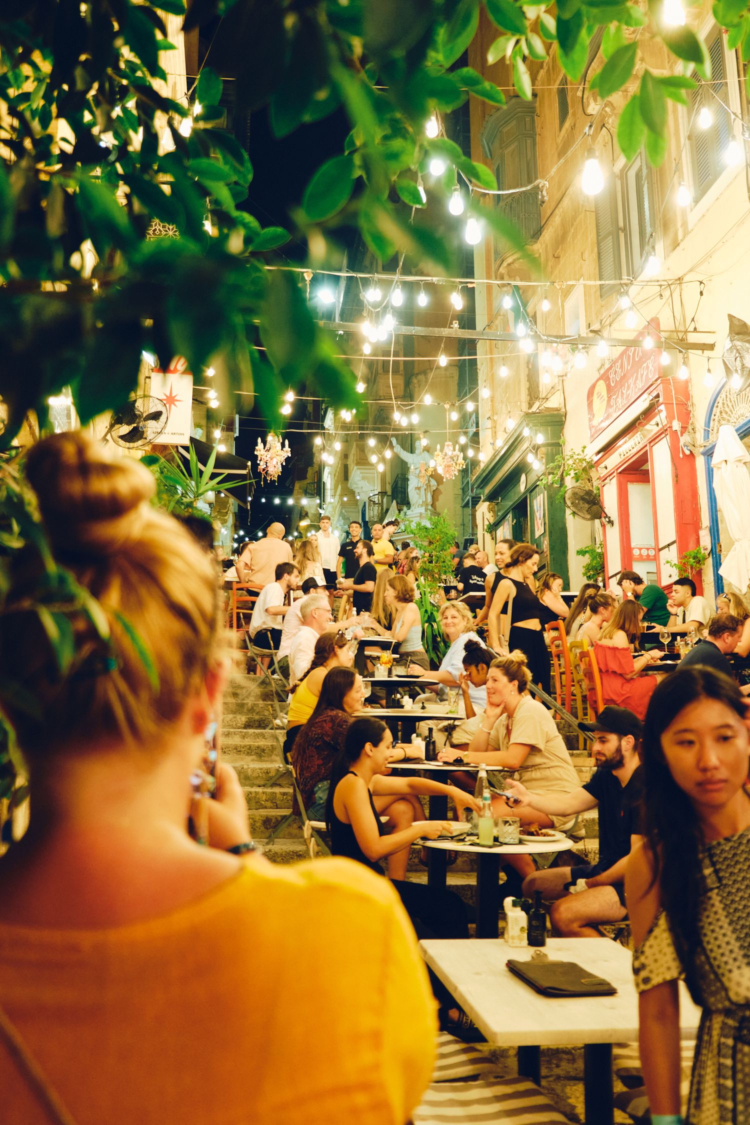 String-lit outdoor restaurant patio filled with diners enjoying a summer evening.