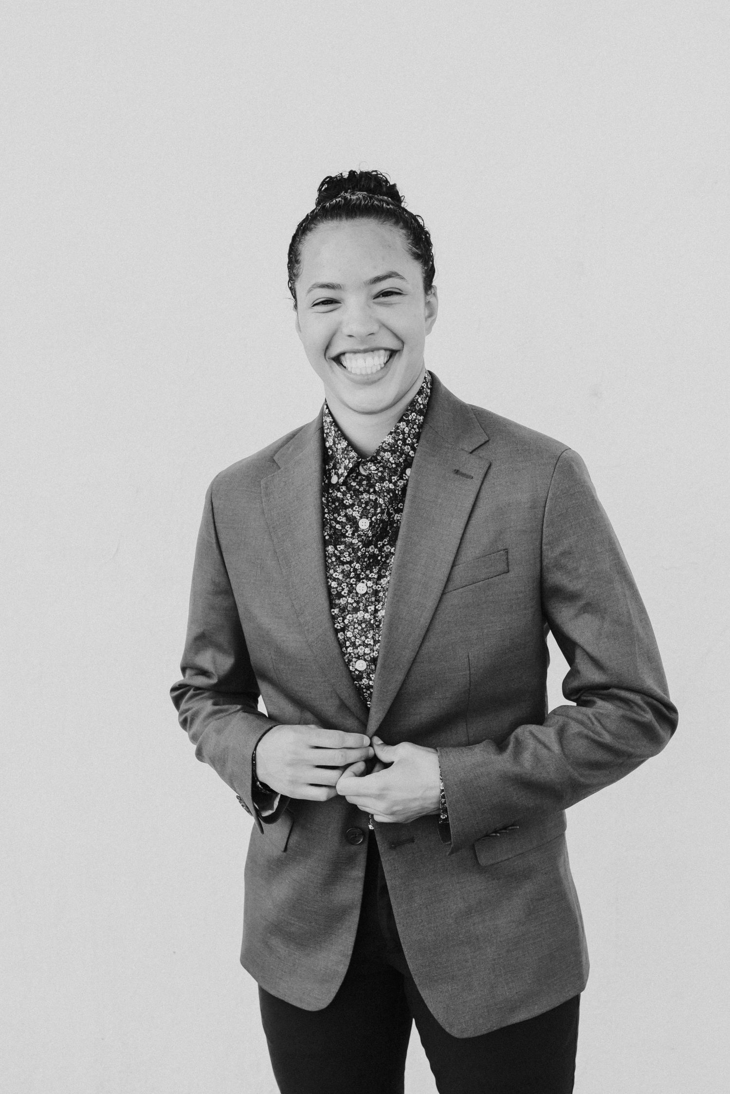 Black and white portrait of someone in a blazer and floral shirt with a cheerful expression.