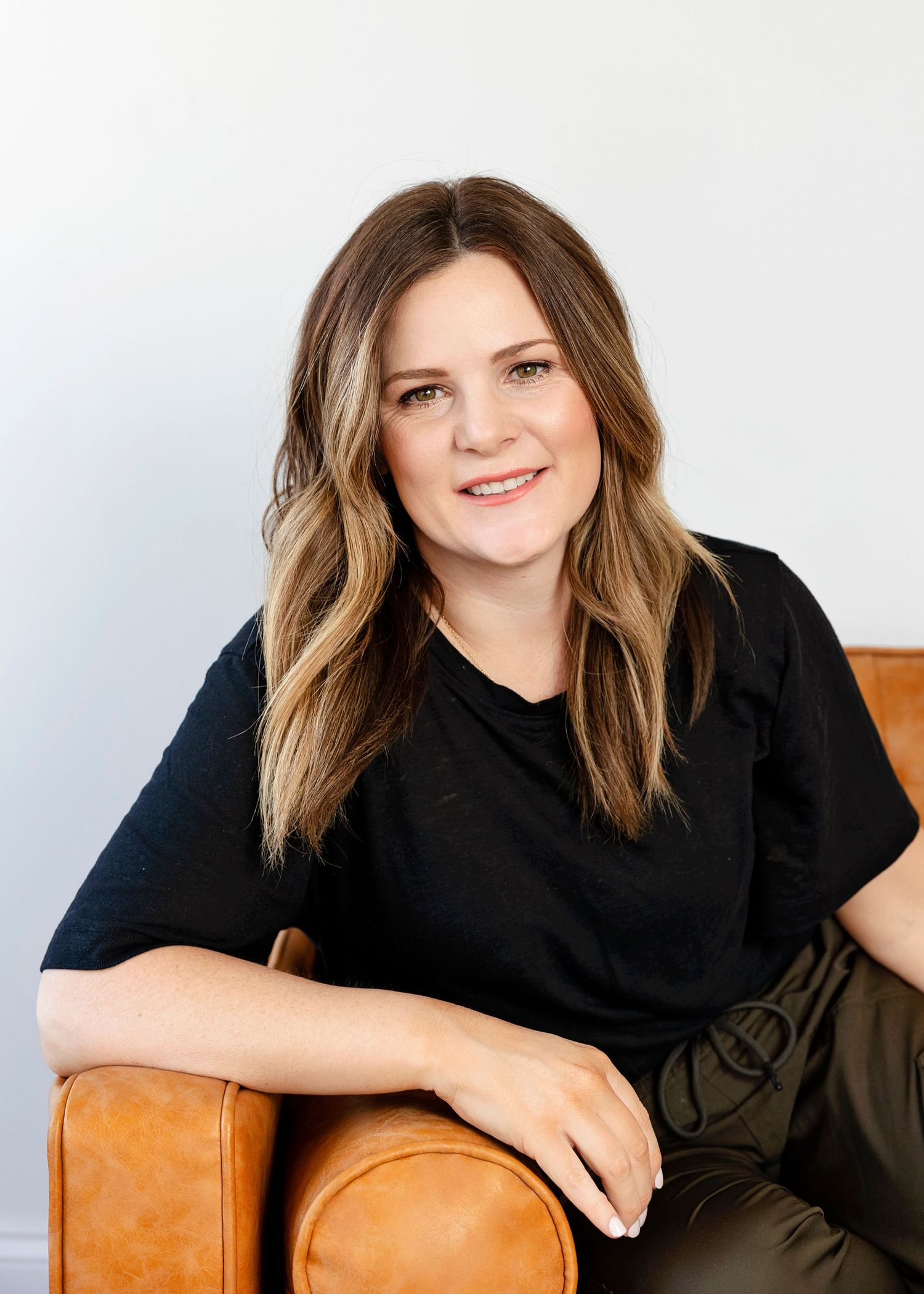 Person sitting casually on brown leather couch wearing black shirt.